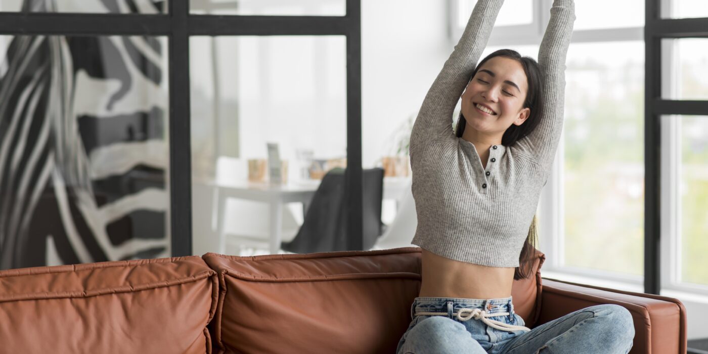 Woman enjoying a peaceful morning stretch on a leather couch inside a bright living room of luxury 4 BHK villa in Mandi Gwal Pahari by CS Realty.